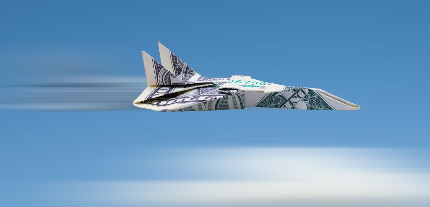 A paper plane made out of a dollar bill soars through the air.