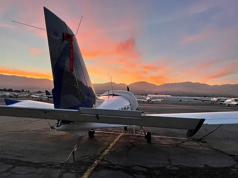 Tail end of an aircraft on the tarmac with pink skies above.