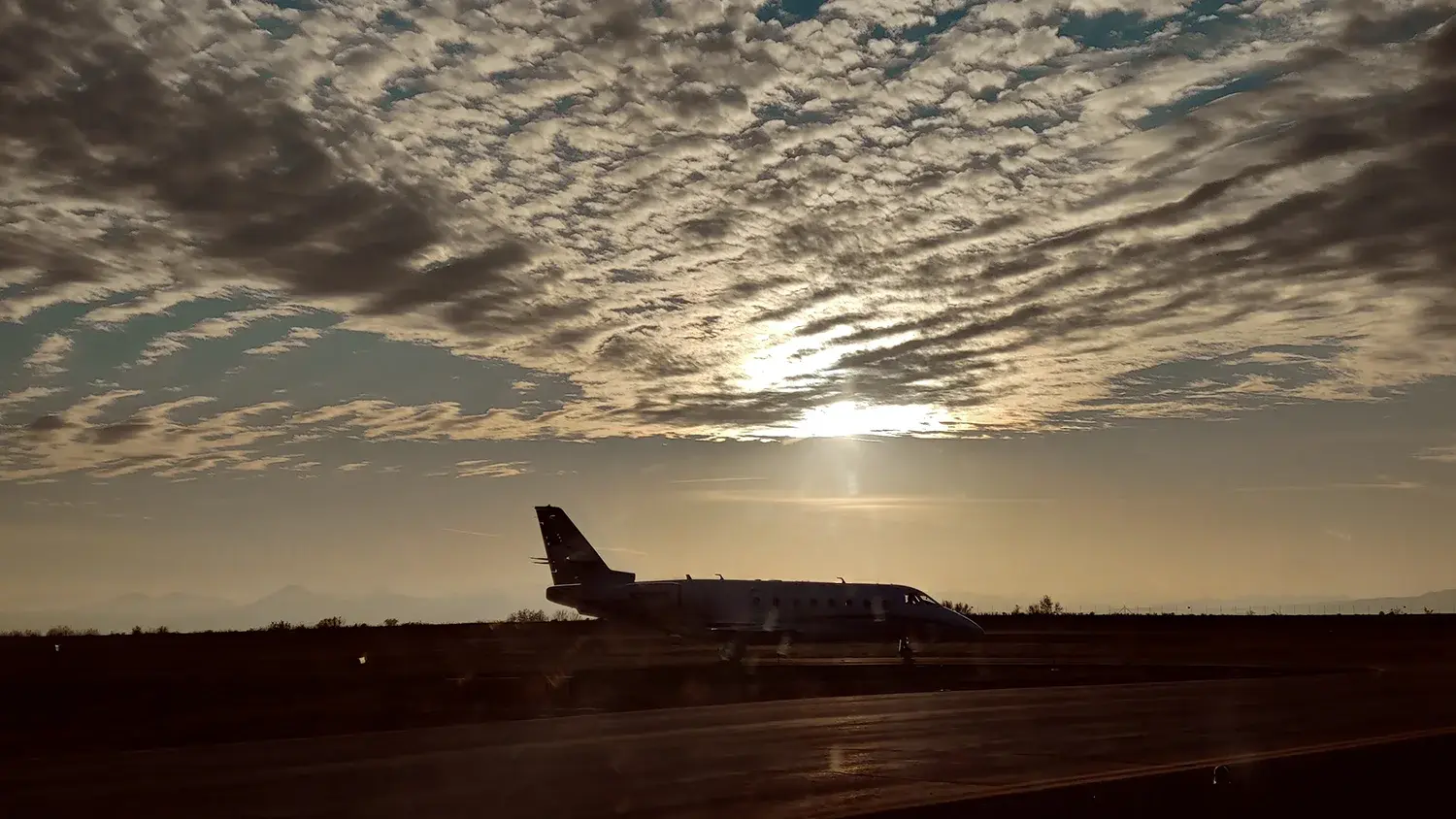 high-contrast photo of an airplane on the tarmac with a sunset and clouds overhead.